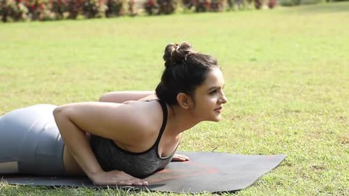 Vidéo stock d'une jeune femme flexible pratiquant l'exercice de yoga Bhujangasana dans un parc.