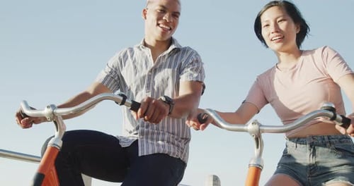 Happy biracial couple riding bikes on promenade, in slow motion