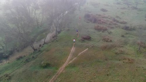 Aerial shot of people running across the field near a river ,competing in a trail race