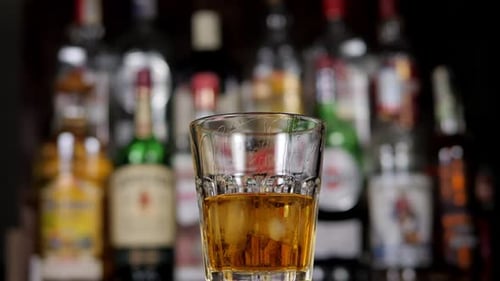 A Closeup of a Glass of Whiskey with Ice Slowly Rotates in the Bar