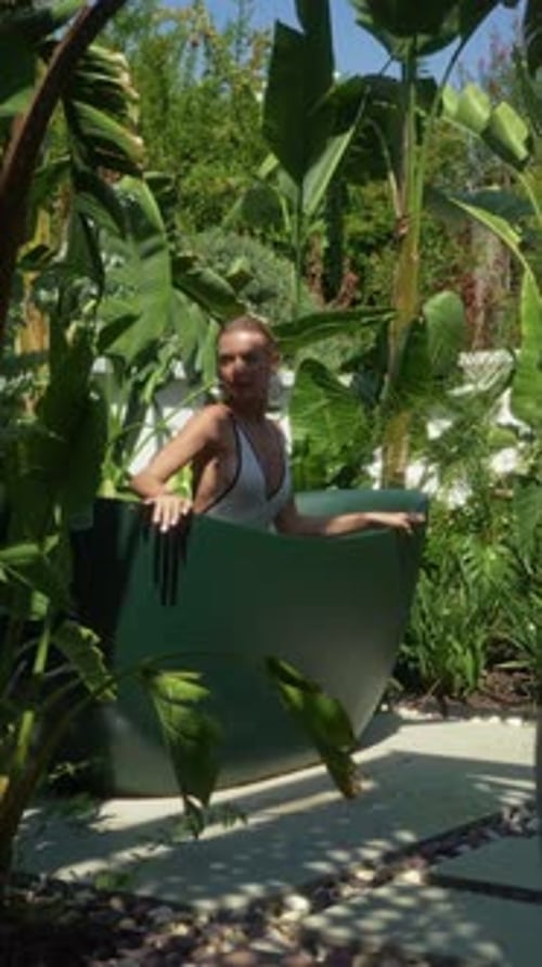 Mulher relaxando em uma banheira ao ar livre cercada por exuberantes plantas e folhagens tropicais