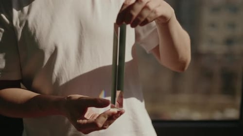 Closeup Cropped Shot of Man Holding and Turning Triangular Glass Prism Refracting Sunlight Into