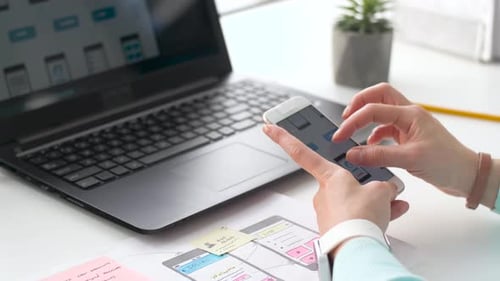 Creative young woman designs mobile app interface on laptop at modern office