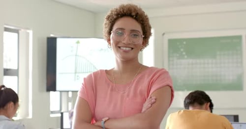 Smiling teacher standing in classroom with students studying in background at high school