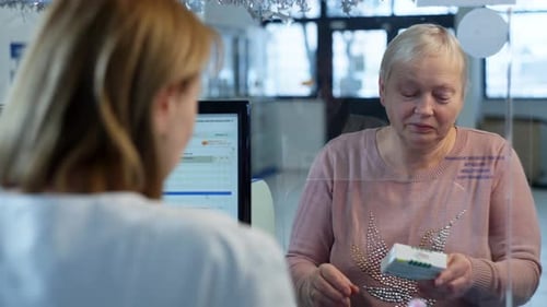 An Elderly Woman Looks at Medicines at the Cash Register in a Pharmacy