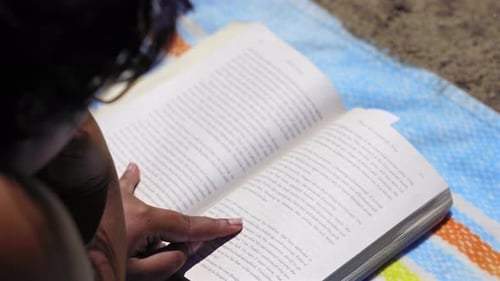 Overhead view of a person engrossed in reading a book on a vibrant beach blanket