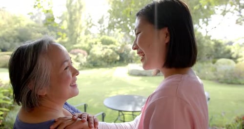 Smiling senior asian woman receiving physical therapy from caregiver in garden