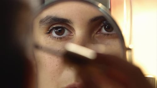 Schöne junge Frau, die Wimperntusche im Spiegel aufträgt. Spiegelbild eines jugendlichen Mädchens, das sich schminkt
