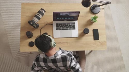 Vista superior de un editor masculino con auriculares que tiene dolor de espalda mientras usa una computadora portátil editando el Vídeo