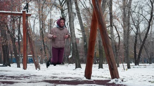 Lady Enjoying Swing on Snowy Winter Day in Playground with Trees in Background