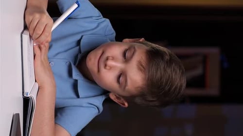 Boy Writes in Notebook at Desk