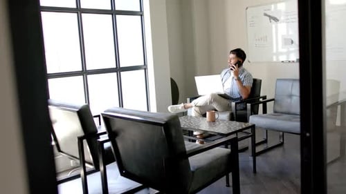 Talking on phone and using laptop, man working in modern office space