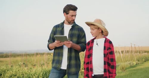 Father and son working on farm. Two farmers man and boy using tablet computer to manage ve getables