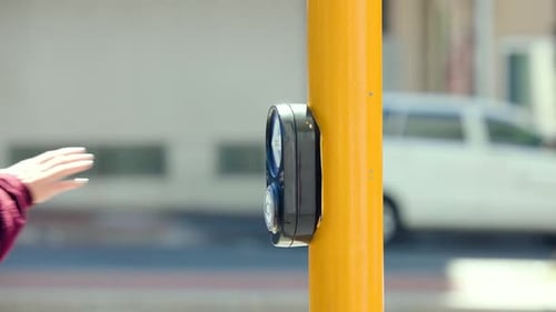 Le bras gauche de la personne dans une manche marron appuie sur le bouton de marche d'un poteau jaune vif, devant traverser