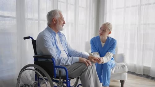 Caregiver Holding Hand of Senior Man in Wheelchair