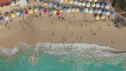Aerial top down view of people on a sandy beach with colorful umbrellas