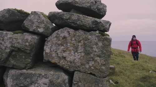 Man in red jacket with backpack on hikes on hills in Nordic landscape with the ocean in the backgrou