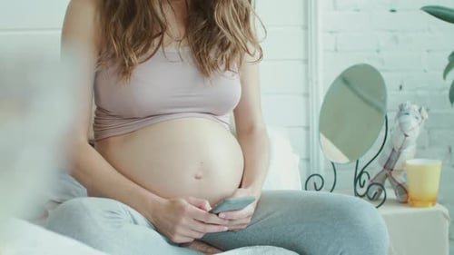 Pregnant Woman Using Smartphone Indoors Sitting on Bed