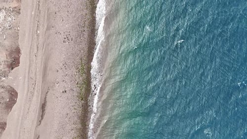 Aerial shot of shoreline with blue ocean and coastal terrain, downward angle drone shot.