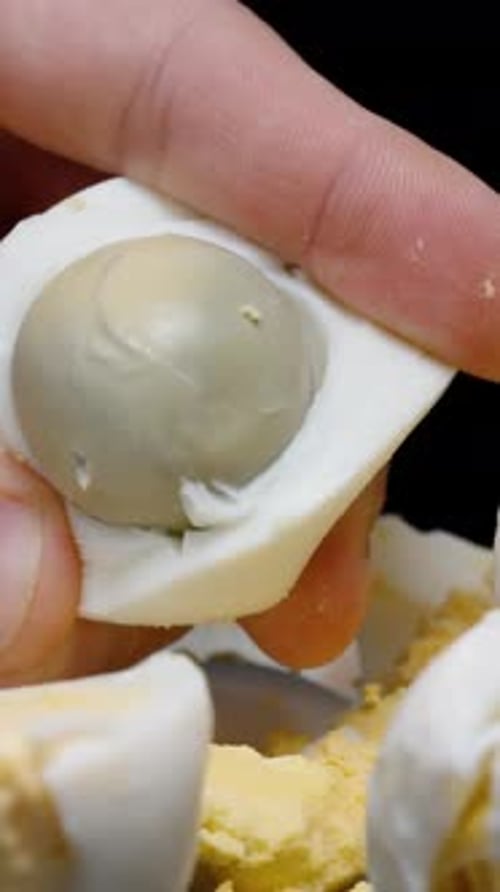 Vertical video. The man takes out the round yolk from the boiled egg. Close-up. Many eggs.