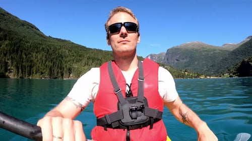 Handsome athletic male with lifejacket and sunglasses is paddling green glacier lake Lovatnet in Nor