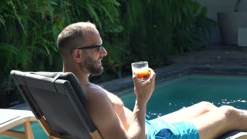 Young Man Relaxing and Drinking Whiskey on Sunbed by Pool 30s
