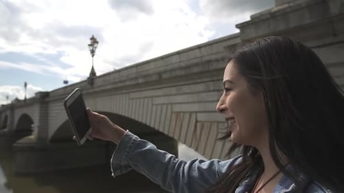Latina tourist using FaceTime and showing her friend the river Thames and Putney Bridge in London, s
