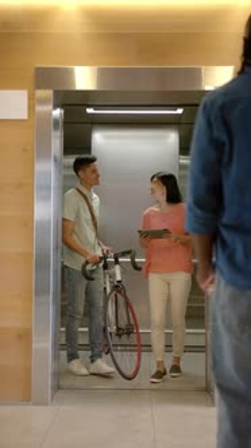 Coworkers Talking Near Elevator in Modern Office