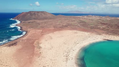 Drone view of Playa De La Concha De Lobos: vast sandy beach curving into turquoise waters, rugged te