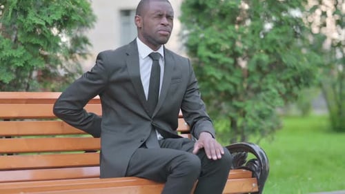 Man in Suit with Back Pain on Park Bench