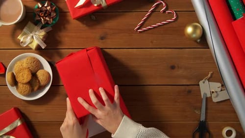 Wrapping Christmas Gift on Wooden Tabletop, Cookies Nearby