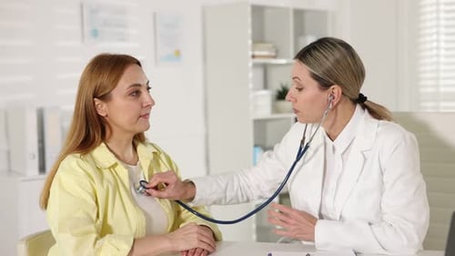 Cardiologist with stethoscope listening patient's heartbeat at table in clinic