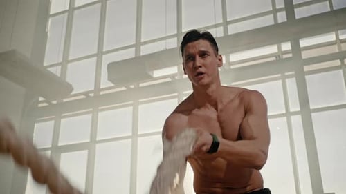 Nahaufnahme in Zeitlupe eines gutaussehenden Sportlers, der mit Battle Ropes in einem verrauchten Fitness-Interieur trainiert