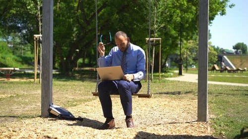 Angry, Upset Businessman On The Swing Throw Away Laptop At City Park