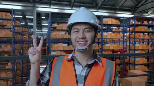 Close Up Of Asian Male Engineer Smiling And Showing Peace Gesture In Warehouse
