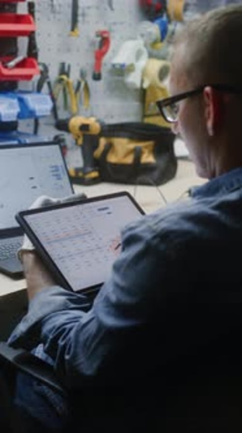 Employee Checking RealTime Stocks Using Digital Tablet and Laptop in Workshop
