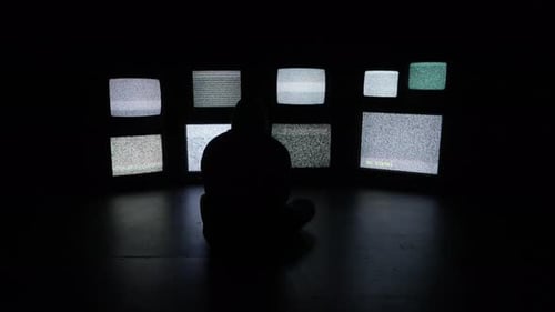 Eine ängstliche und isolierte Person sitzt vor einer Wand aus weißem Rauschen gefülltem Fernseher und Medienbildschirm
