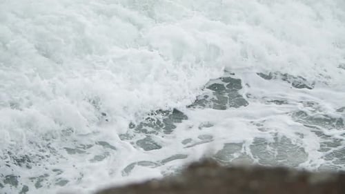 Slow motion wave foam in tight shot with rock in the foreground.