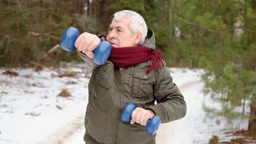 Homem sênior malhando ao ar livre na floresta de inverno, pessoa levantando halteres, homem velho se exercitando