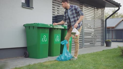 Caucasian Man is Walking Outside His House in Order to Take Out Two Plastic Bags of Trash. One Garb