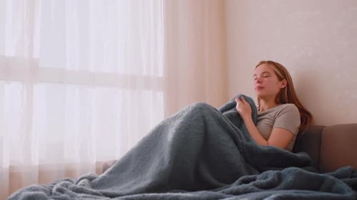 Young Woman Seated on Sofa Covering Herself with Blanket
