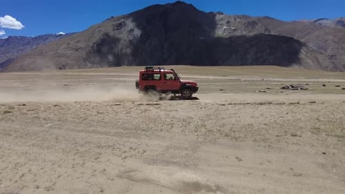 Red Vehicle Driving Across Arid Mountain Landscape