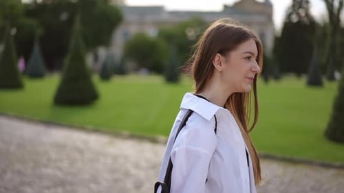 Slow Motion A Young Smiling Girl with Long Hair Walks Through a City Park on a Sunny Summer Day