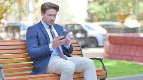 Man in Suit Uses Cellphone on Park Bench