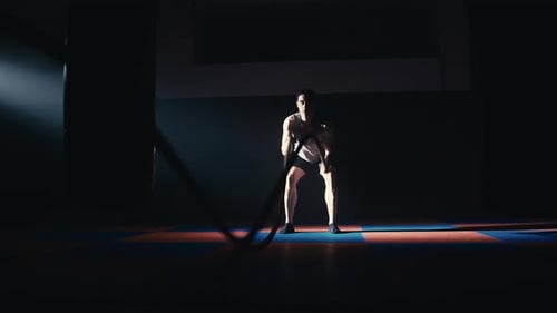 Man Training with Battle Ropes in Dark Gym