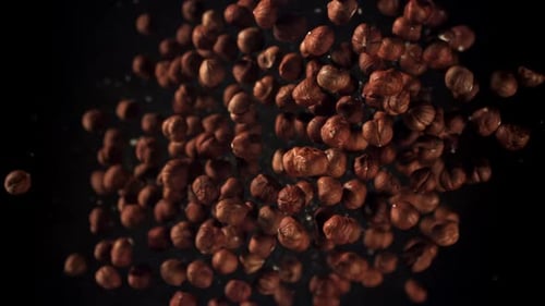 Peeled Hazelnuts Falling Against Dark Background