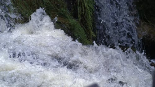 Close-up of splashing waterfall foam against mossy rocks and grass in Ultra slow motion captured