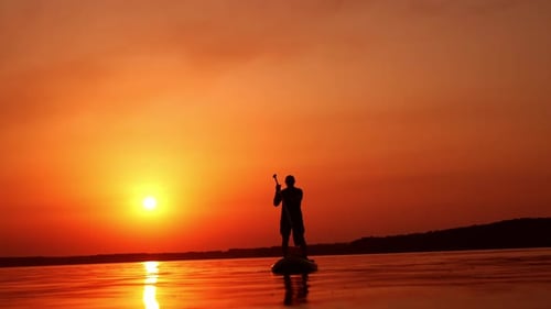 Approaching black male silhouette on the sup board. Man practicing on the river at sunset in summer.