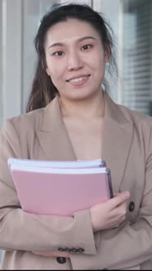 Female University Student Holding Folders and Looking at the Camera While Standing at the Hallway