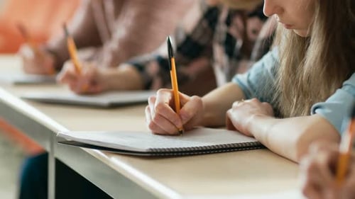 Close-up of the Row of Students Writing in the Notebooks, Taking Exam. Focus of Hands with Pens.